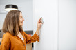 © rh2010 - Young woman regulating heating temperature with a modern wireless thermostat installed on the white wall at home. Smart home heating regulation concept