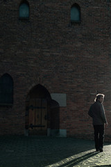 Man in green jacket walking on pavement near church.