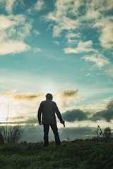 Man with handgun in countryside at sunset.