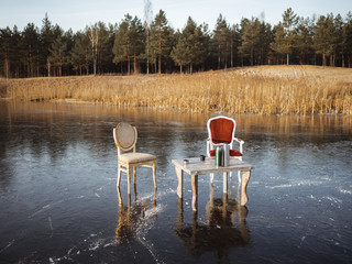 Old vintage table, two chairs stand on the ice of a forest lake