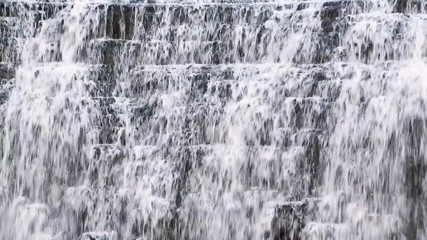 Wall Mural - Water splashes and cascades down a beautiful waterfall flowing over a rock face in this seamless video loop