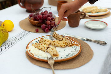 Woman's  hand with fork under plate with pancakes on a table with white tablecloth