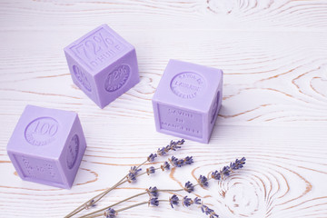 Natural lavender soap of a cubic form of lilac color with the inscription in French: Marseille lavender soap, 100 grams, and lavender flowers on a white wooden table, rustic style