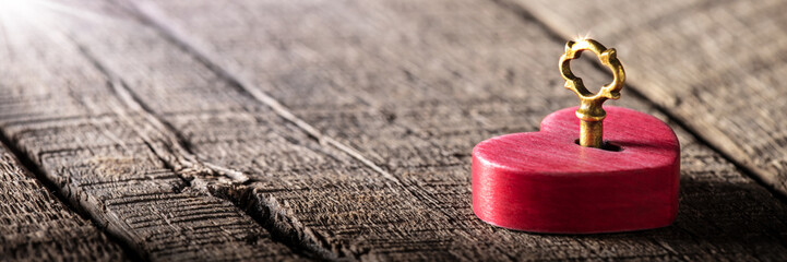 Wall Mural - small rustic red heart with shiny golden key laying on wooden table - valentine's day concept