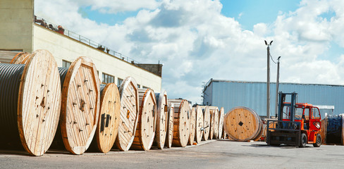 Reels with electrical power cables at the supplier’s warehouse. Wire on wooden coils. Forklift on background using for transportation and move the reel of electrical power wire