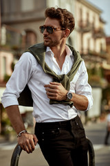 Wall Mural - Stylish man wearing sunglasses and white shirt with tied sweater on shoulders