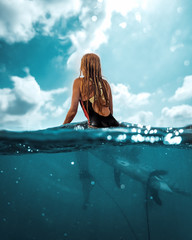 Happy blonde european girl seating on surfboard in the ocean at summer time, shot from the water half in - half out 