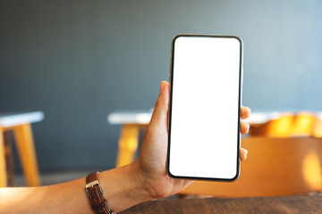 Mockup image of a hand holding and showing black mobile phone with blank screen in cafe