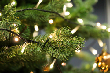 Christmas tree branches close up decorated with garland lights. Festive holiday background with artificial fir tree. Blurred backdrop