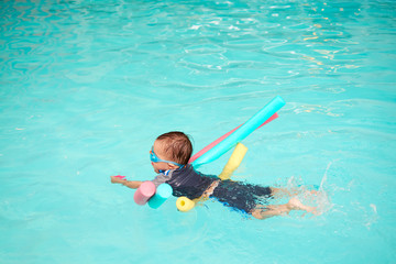 Wall Mural - Asian 2 - 3 years old toddler boy child take swimming class, kid learn to float with pool noodle alone, Kid holding toy and kicking his legs in indoor swimming pool