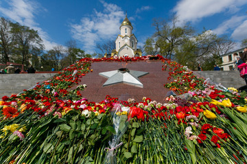 Wall Mural - The eternal flame in Vladivostok. Beautiful bouquets of red flowers lie by the eternal flame against the background of an Orthodox church.