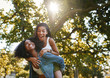 Portrait of a excited young woman enjoying the piggyback ride on her african american friend's back in the park having fun and laughing 