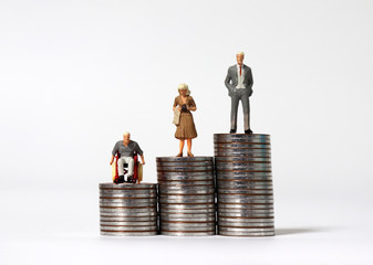 Wall Mural - A miniature man in a wheelchair and a miniature man standing with a miniature woman standing on a pile of coins. The concept of wage differentials.