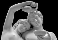 The Marble Sculpture Of Young Roman Couple . Close Up Of A Sculpture Of A Man And Women Gazing Lovingly Into Each Others Eyes. Young Naked Roman Woman And Man In Unity Isolated On Black Background