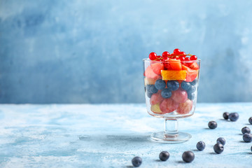 Glass with tasty fruit salad on color background