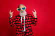 Photo of funky aged man amour cupid character role showing horns fingers excited emotions wear sun specs hearts pattern suit costume shirt tie isolated red color background
