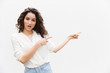 Pensive flirty woman pointing fingers away at copy space. Wavy haired young woman in casual shirt standing isolated over white background. Advertising concept