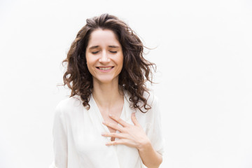 happy grateful pretty woman with closed eyes applying hand to chest. wavy haired young woman in casu