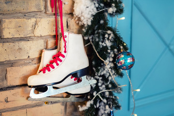 Pair of white vintage leather skates with red laces hanging on old rustic brick wall with garland lights on christmas tree decoration. Cozy scenic christmas card interior winter holidays background