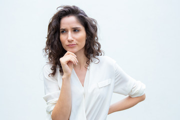 Pensive female customer touching chin, looking away, thinking hard. Wavy haired young woman in casual shirt standing isolated over white background. Advertising concept