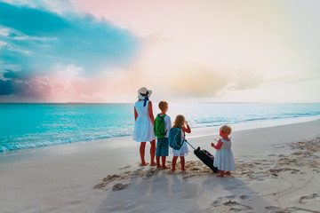 mother with kids with backpacks and suitcase travel on beach