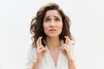 anxious woman keeping fingers crossed and praying for luck. wavy haired young woman in casual shirt 