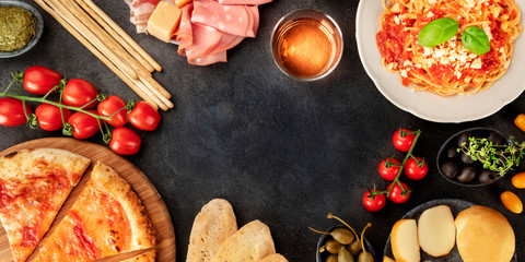 Wall Mural - Italian food panorama with copy space. Pizza, pasta, cheese, ham, wine, olives, pesto, capers, shot from above forming a frame with a place for text, a flatlay design template on a black background