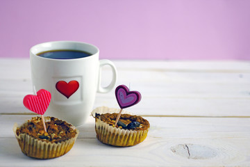 Canvas Print - Valentine's Day breakfast. White mug of tea with a heart pattern and and two homemade cupcakes with candle hearts on a pink background. Copy space