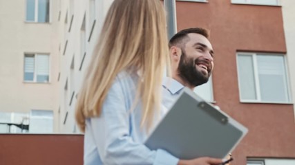 Wall Mural - Smiling young office colleagues talking and walking with clipboard and cup of coffee outdoors