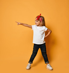 Wall Mural - Cheerful kid girl in white blank t-shirt, blue jeans and red headband pointing her finger looking to the side on yellow