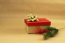 Gift Box With Red Top And Gold Bow With A Branch Of Christmas Tree On Brown Background