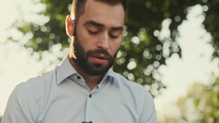 Poster - Close up view of calm bearded businessman answering the call and becoming unhappy while sitting in park outdoors