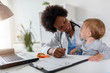 © lordn - Smiling female afro american doctor general practitioner talks and amuses small child before medical examination