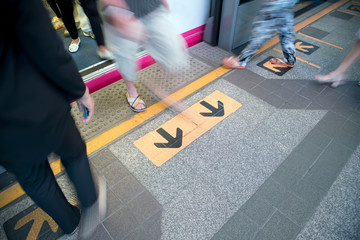 Motion blured of legs of  people walking from sky train to platform with sign or symbols of two black-yellow back arrows, Bangkok, Thailand.