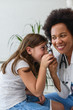 © lordn - Smiling female afro american doctor general practitioner talks and amuses child before medical examination