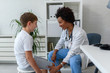 © lordn - Woman African American doctor general practitioner examining child's patellar knee-jerk reflex