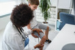 © lordn - Woman African American doctor general practitioner examining child's patellar knee-jerk reflex