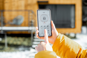 holding phone with launched alarm app on the house background outdoors. concept of controlling and m