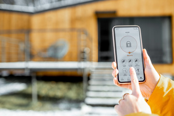 Holding phone with launched alarm app on the house background outdoors. Concept of controlling and managing home security from a mobile device