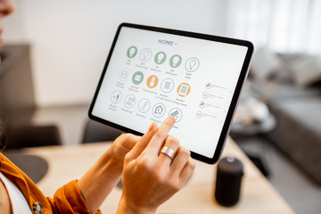 Young woman controlling home with a digital touch screen panel. Concept of a smart home and mobile application for managing smart devices at home