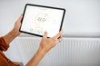 © rh2010 - Controlling radiator heating temperature with a tablet, close-up with radiator on the background. Concept of a smart home and mobile application for managing smart devices at home