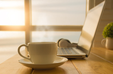 Breakfast with a cup of warm coffee on the table in the office which has a laptop. And headphones are placed for listening to relaxing music.