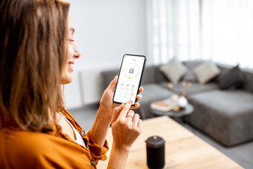 young woman holding smart phone with launched security application at home. concept of controlling a