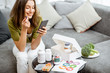 Woman taking nutritional supplements in the form of pills while sitting with smart phone at home. Concept of individual online selection of food supplements. Preventive medicine