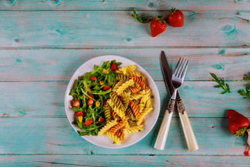 Italian pasta salad with fresh strawberry and green salad on wooden rustic background. Top view