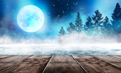 Winter background. Winter snow landscape with wooden table in front. Dark winter forest background at night. Snow, fog, moonlight. Dark neon night background in the forest with moonlight. 