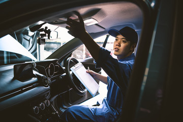 Mechanic holding clipboard and checking inside car to maintenance vehicle by customer claim order in auto repair shop garage. Repair service. People occupation and business job. Automobile technician