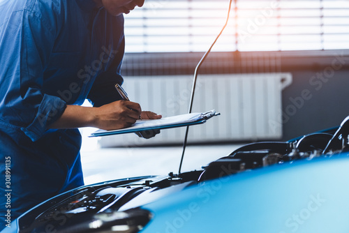 Fotomural Car mechanic holding clipboard and checking to maintenance vehicle by customer claim order in auto repair shop garage