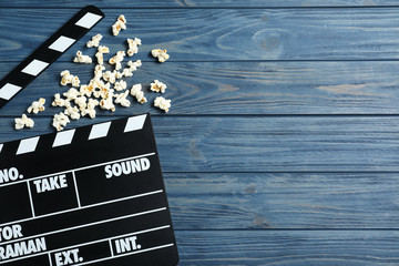 Clapper board and popcorn on blue wooden background, top view with space for text. Visiting cinema
