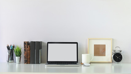 Workspace contemporary laptop empty screen, books, pencil, coffee and photo frame with alarm clock.